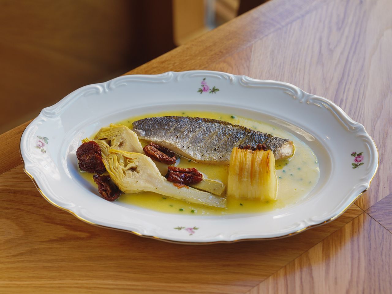about-us A gourmet plate featuring fresh fish, artichokes, and sun-dried tomatoes beautifully presented.