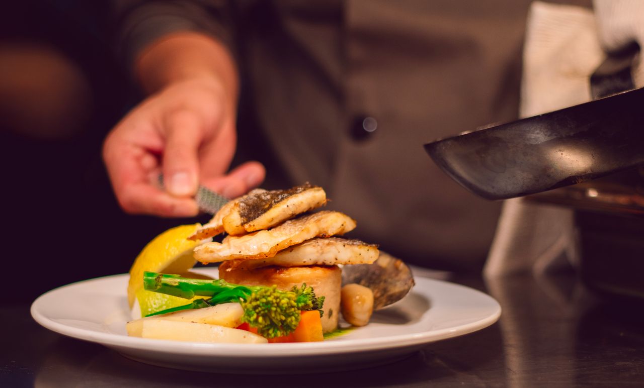 who-we-are Gourmet fish dish with vegetables being served by a chef in a UK restaurant.