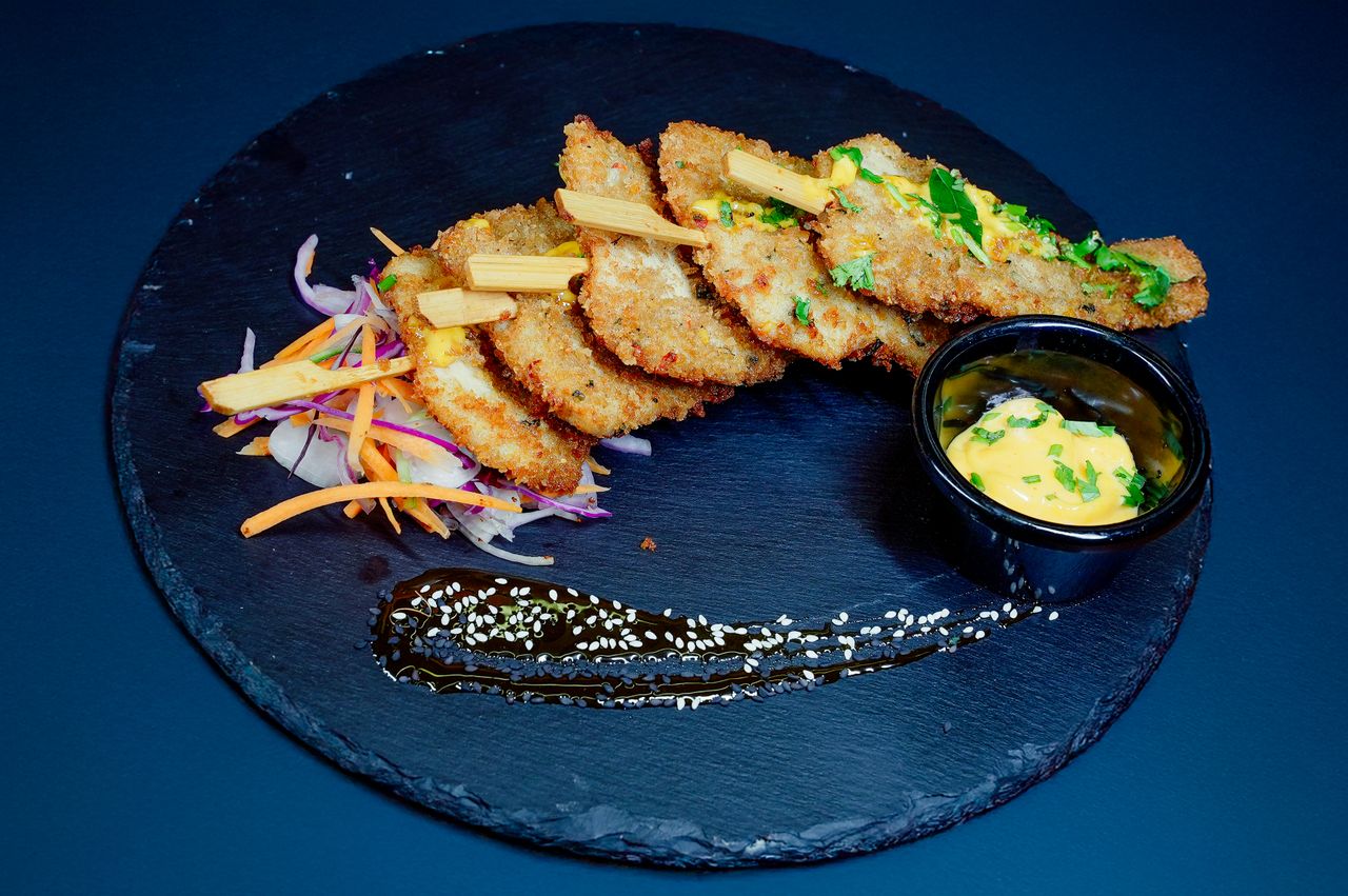 Elegant presentation of crispy chicken filets with sauce and vegetables, arranged on a slate platter.