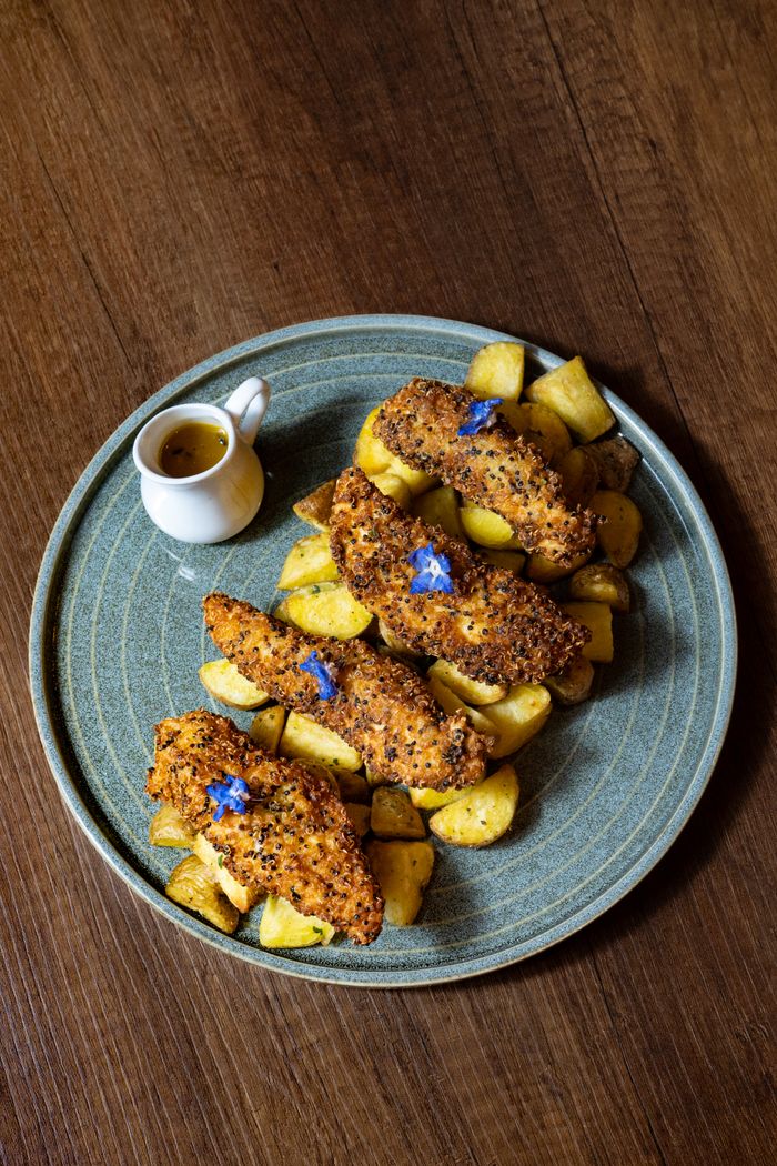 services-04 A tantalizing dish of crispy breaded fish atop roasted potatoes with a side of sauce.